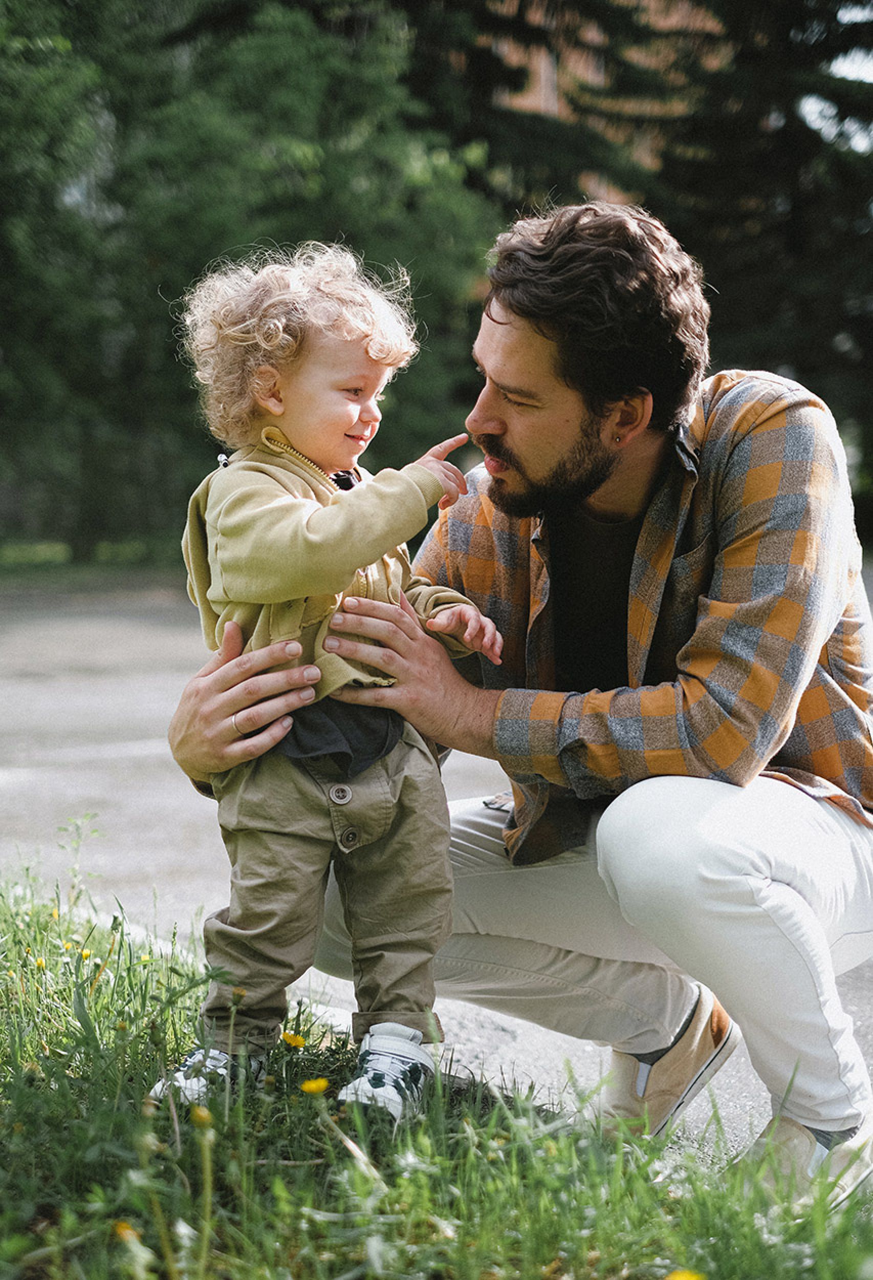 Small toddler boy stands next to his father and touches his nose