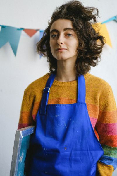 Close up of woman in bright striped sweater and blue apron holding a canvas